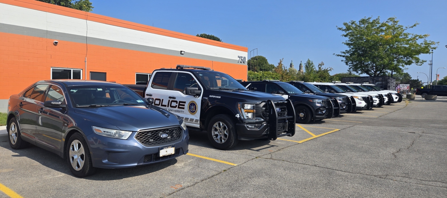 Image of orange building with a row of eight police vehicles parked in front of it, all facing outward.